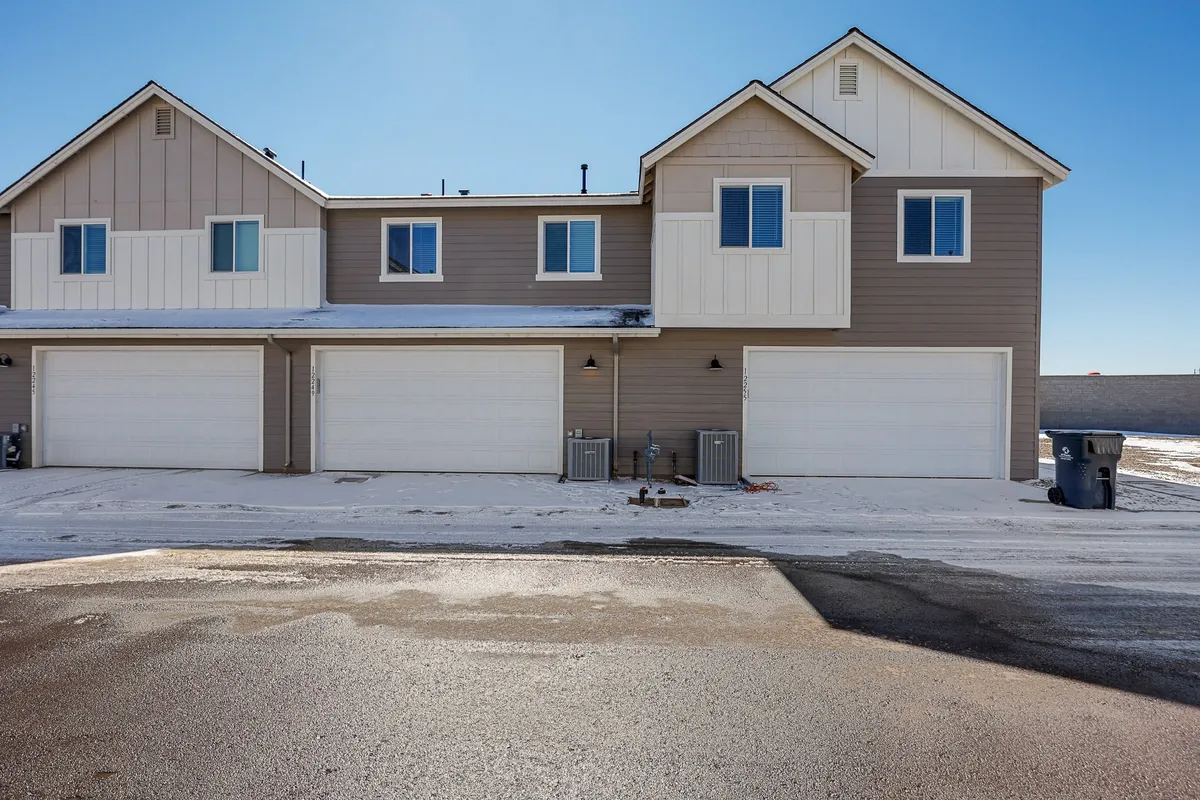 This exterior image showcases the front of a two-story duplex, complete with garage doors and front pathways leading up to welcoming entrances. The scene hints at a quiet neighborhood, and the open space around the property suggests a tranquil setting for outdoor activities or evening sky watching.
