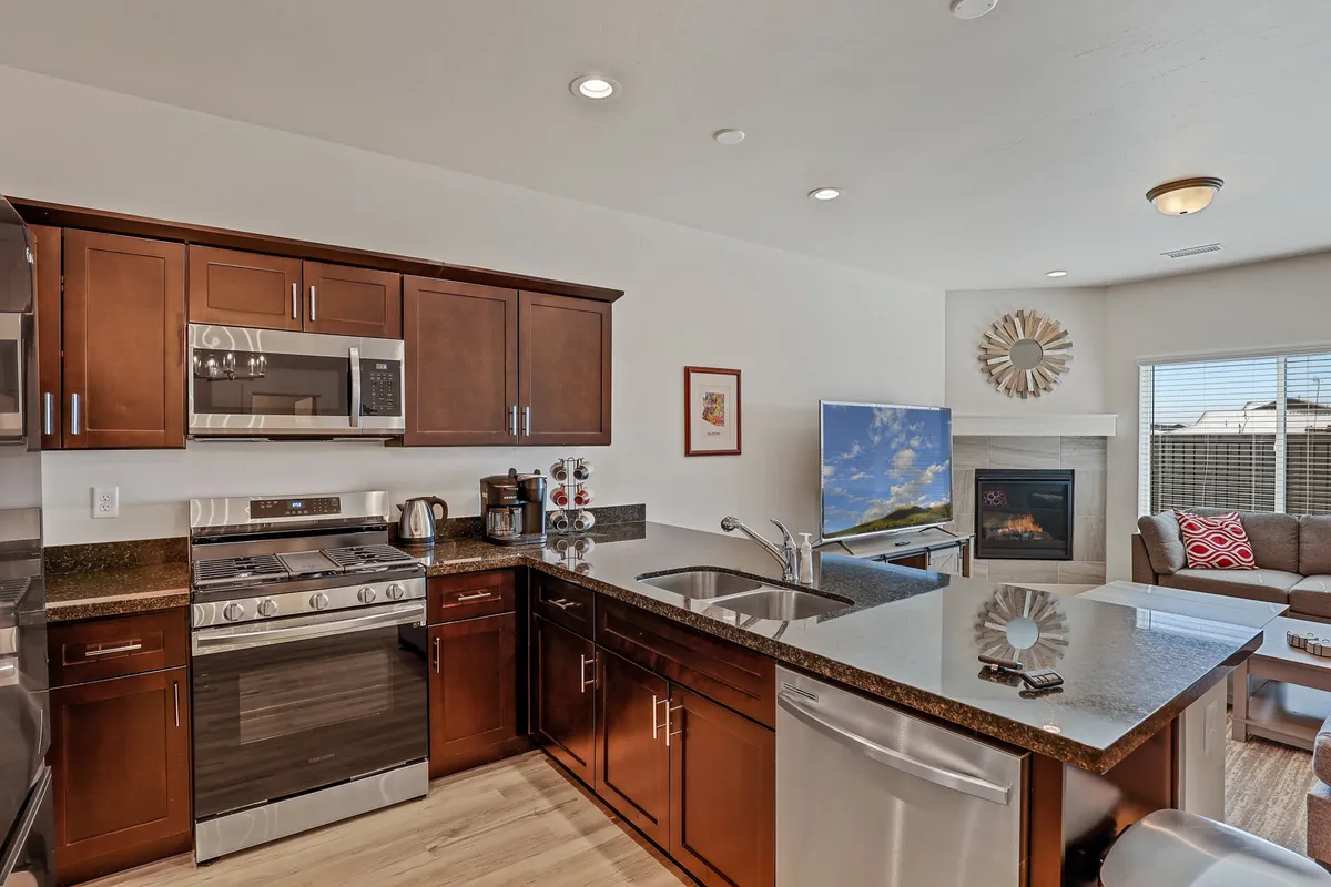 A spacious and inviting living area featuring a comfortable seating arrangement facing a modern fireplace and a prominent TV, with a kitchen island visible in the background. The scene evokes a sense of togetherness, ideal for group gatherings, entertaining, and relaxing after a day out.