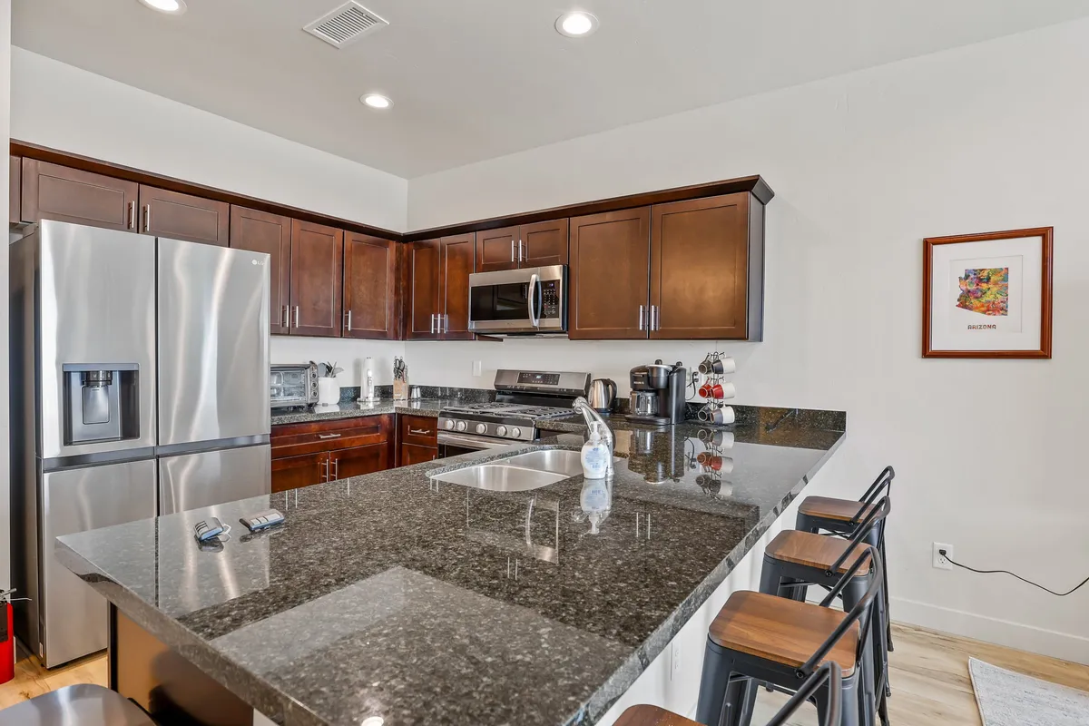 A welcoming kitchen with granite countertops, stainless steel appliances, rich wood cabinetry, and bar stools tucked under the breakfast bar. The scene captures a sense of warmth and functionality, ideal for morning coffee or meal prep.